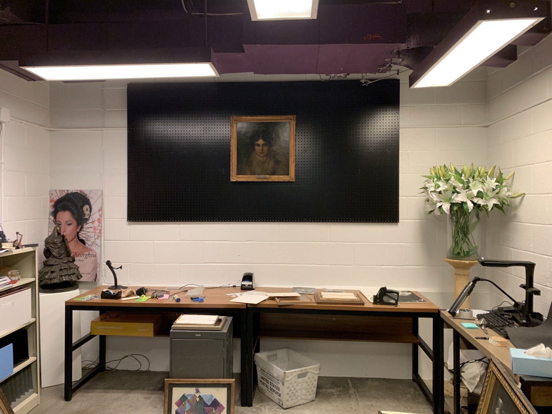 A workspace with art and supplies. A framed painting hangs on a black pegboard, table with supplies.