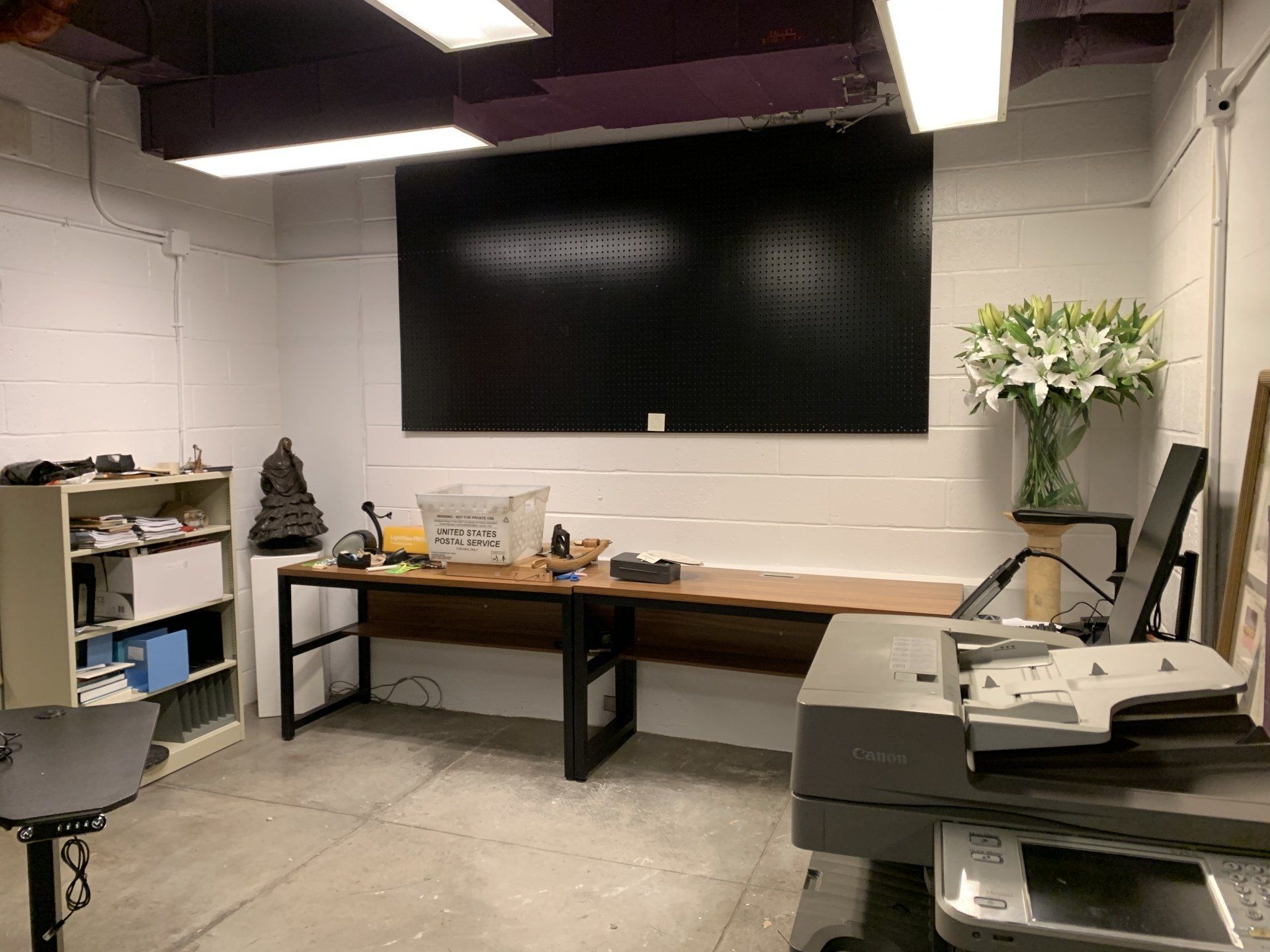 Home office with a desk, printer, large chalkboard, and a vase of white flowers.