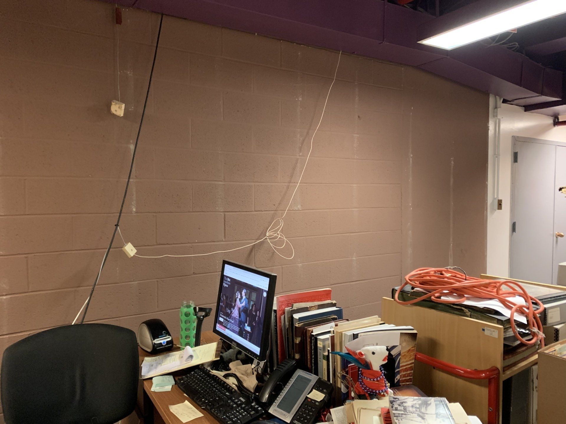 Office workspace with a computer, cords on the wall, and a cluttered desk.