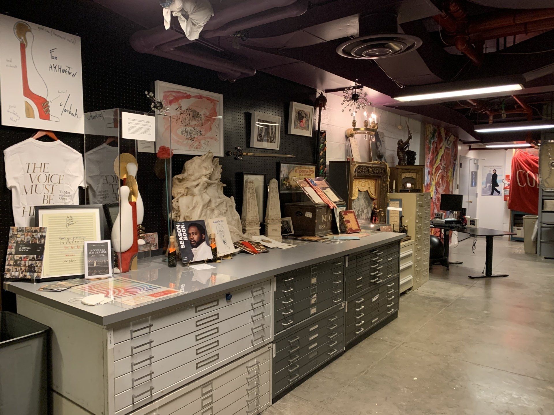 A cluttered art studio: drawings, statues, and framed items displayed on a counter and walls.