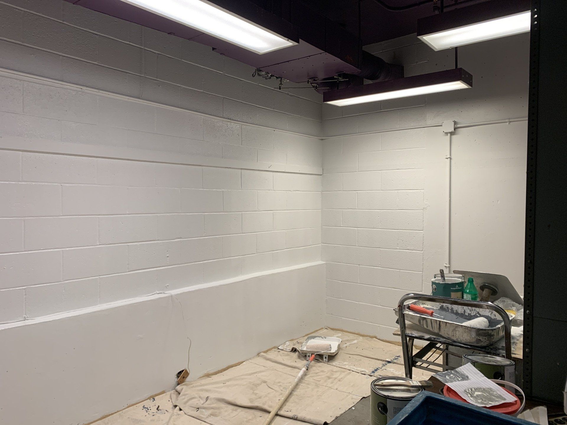 Empty room with white brick walls, fluorescent lights, and a painting supplies cart.