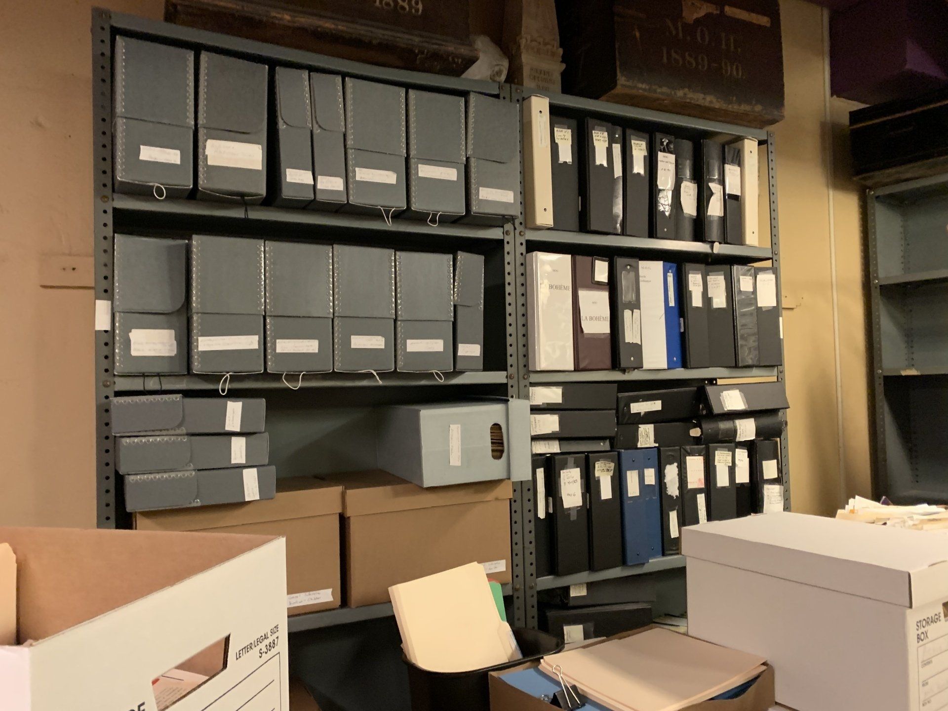 Shelves of gray archival boxes and file folders in a storage room.