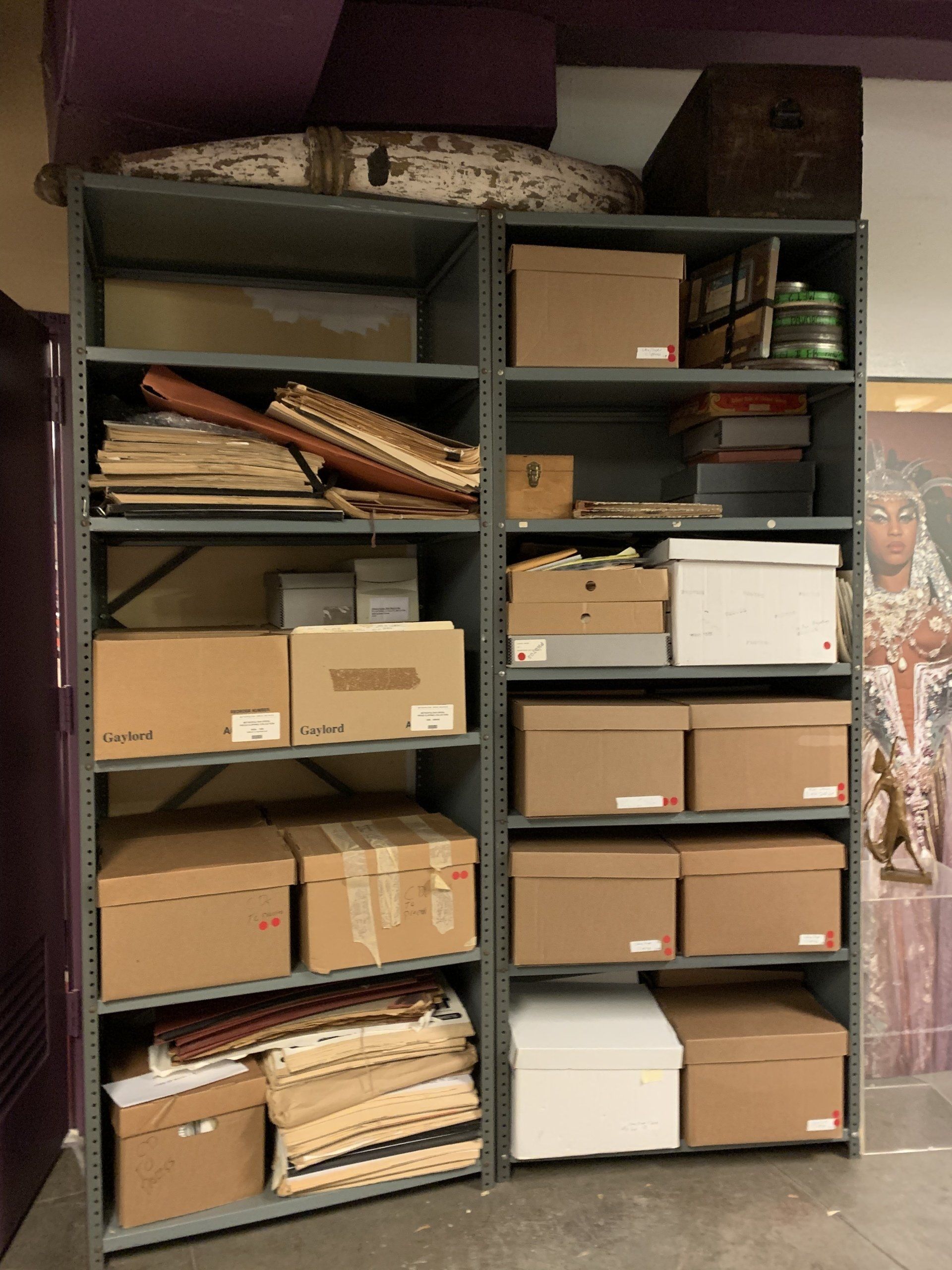Two metal shelves filled with cardboard boxes and various artifacts in a room.