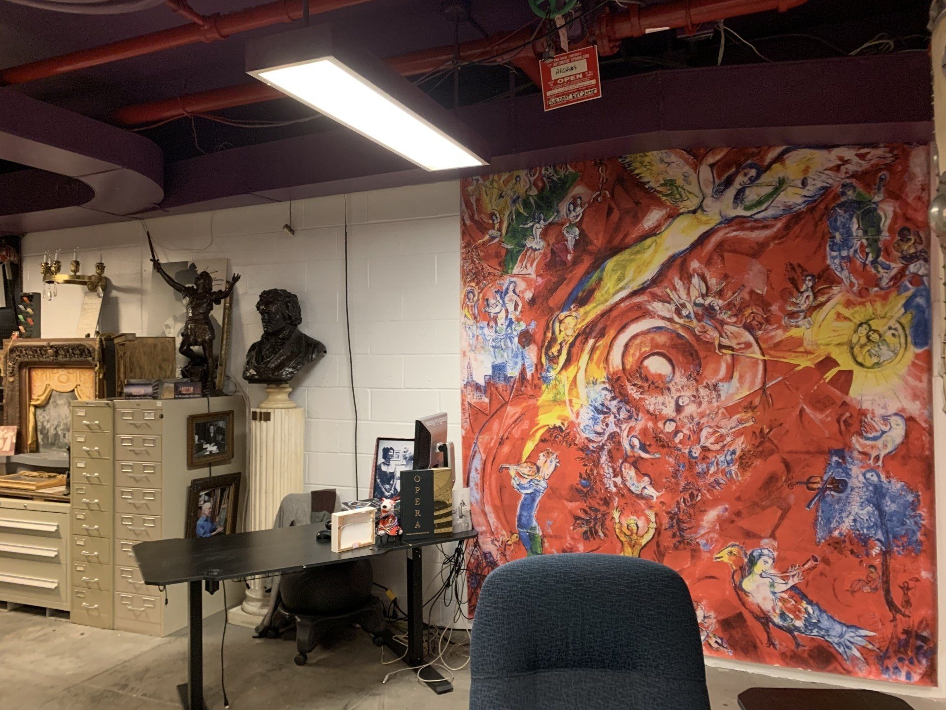 A room with a large red Chagall-style artwork, desk, bust, and file cabinets.