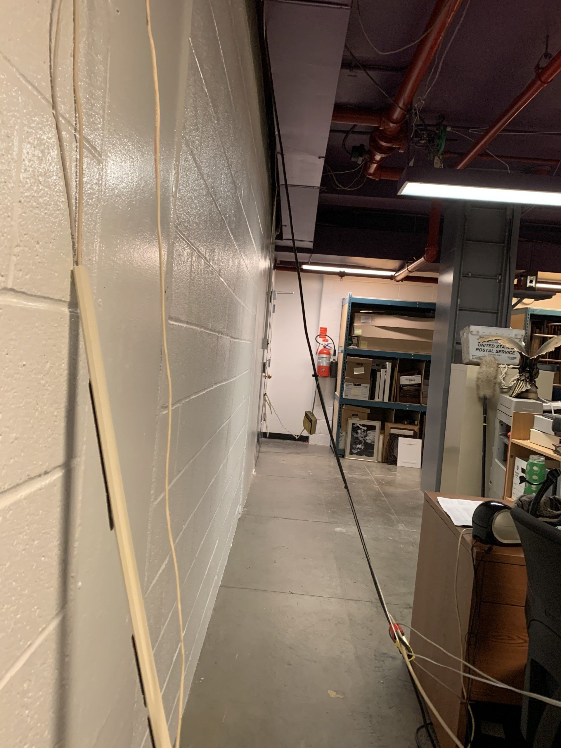 A narrow, white-walled hallway with a black cable hanging down. A door is visible at the end.