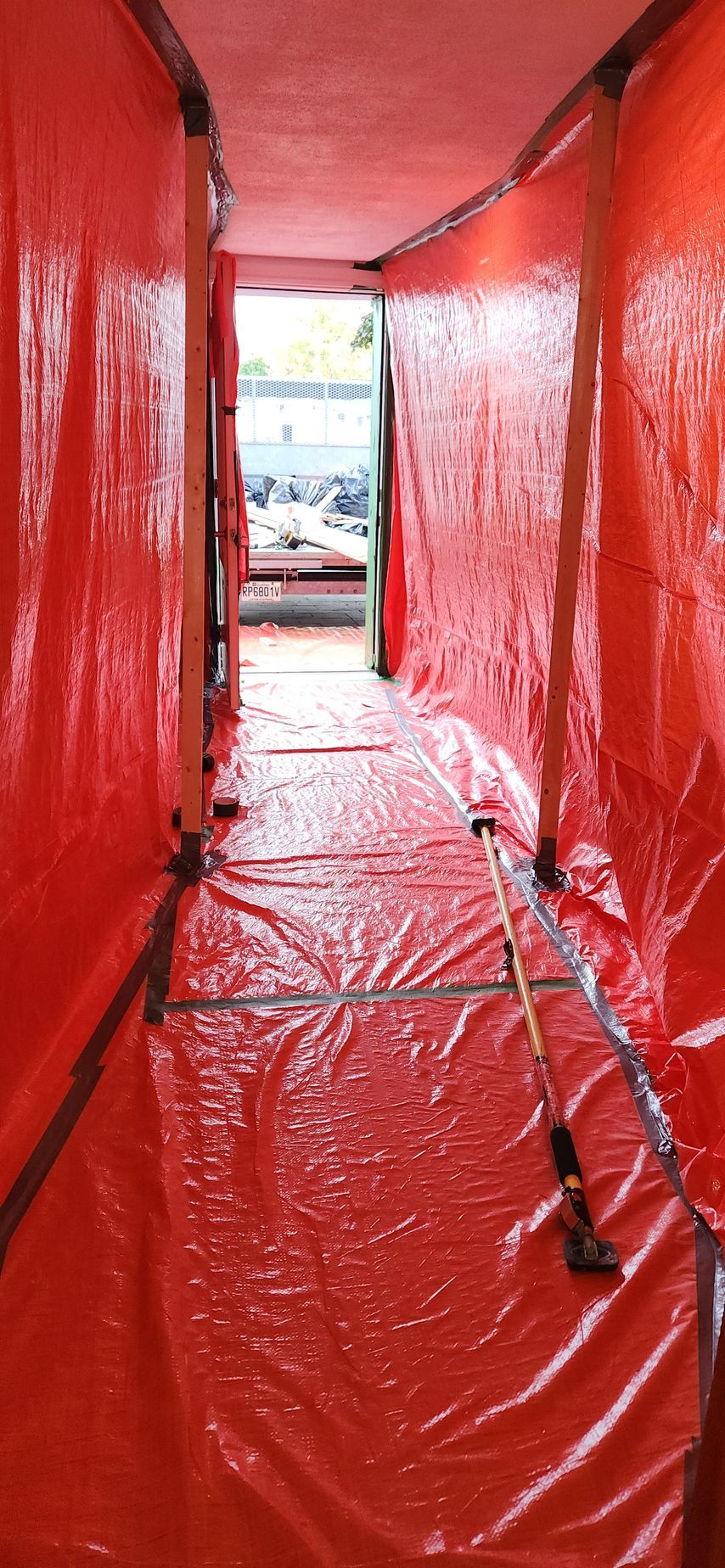 Un couloir recouvert d'une bâche rouge, menant à une porte ouverte avec une canne à pêche au centre.