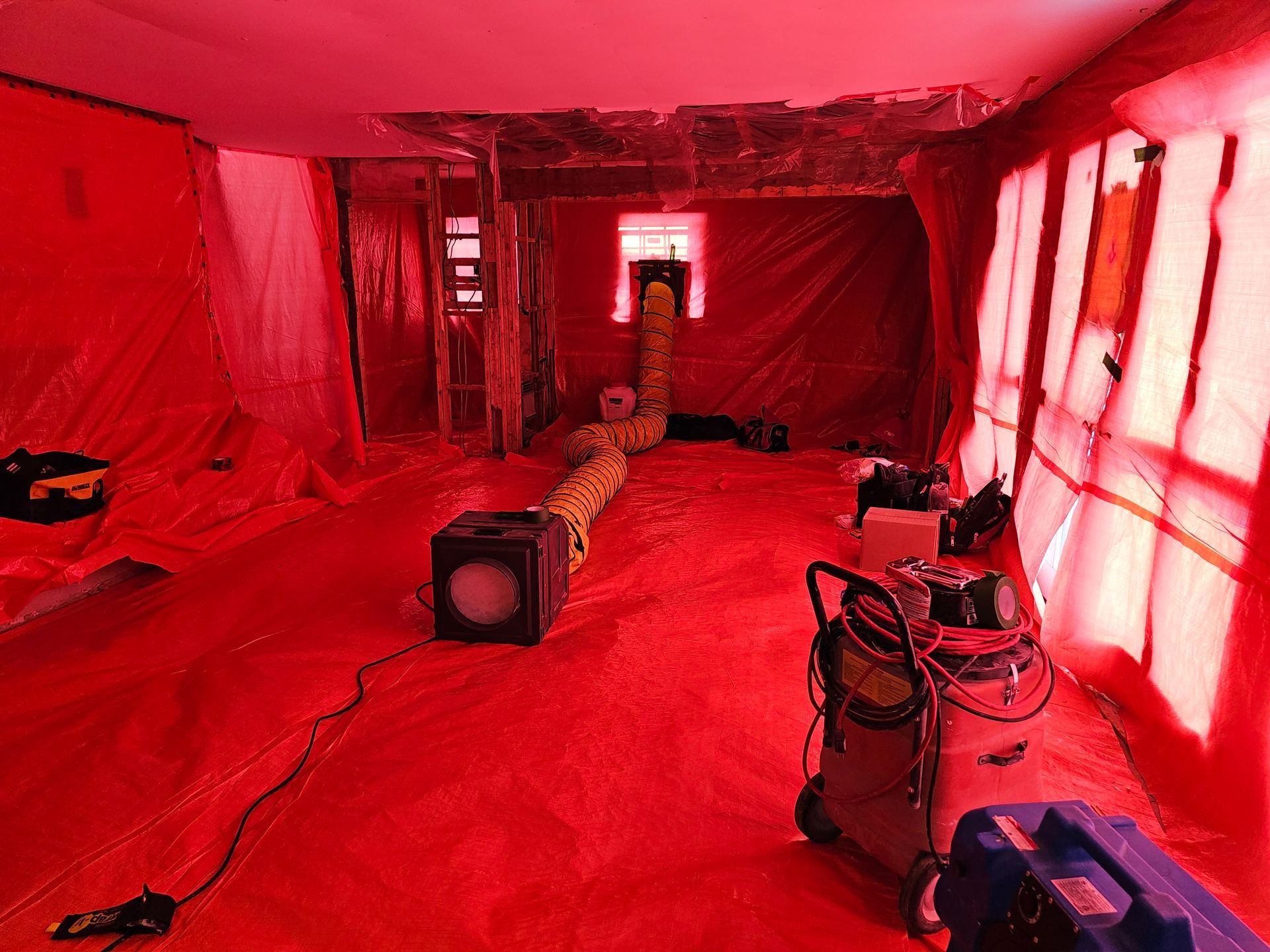 Espace intérieur recouvert d'une bâche en plastique rouge ; équipement de filtration d'air en fonctionnement.