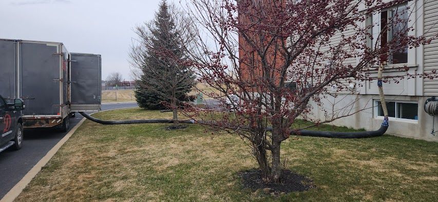 Une remorque de camion noire avec un tuyau, reliée à un bâtiment devant lequel se trouve un arbre.