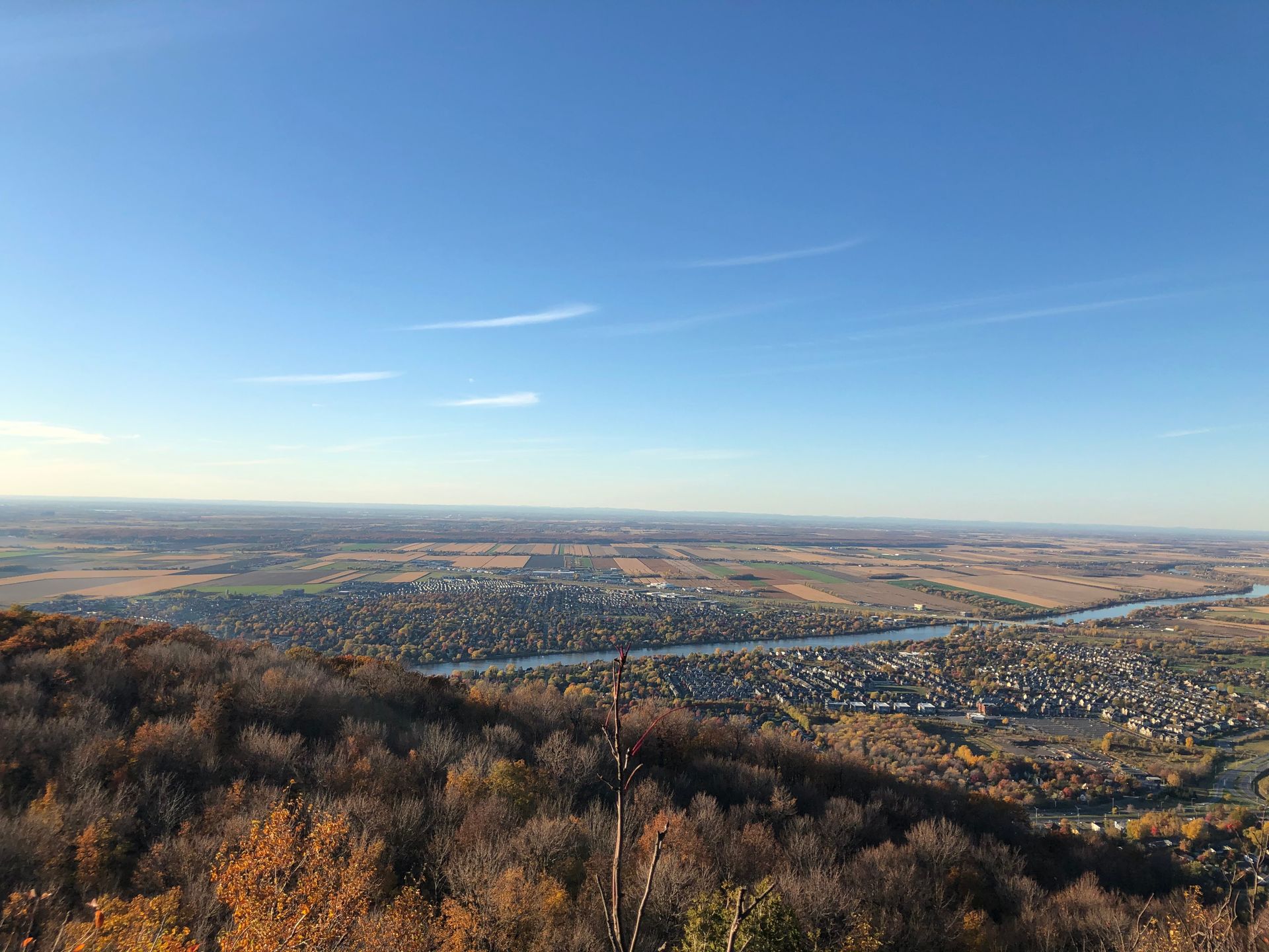 Vue panoramique sur une ville et une rivière serpentant dans une vallée sous un ciel bleu limpide.