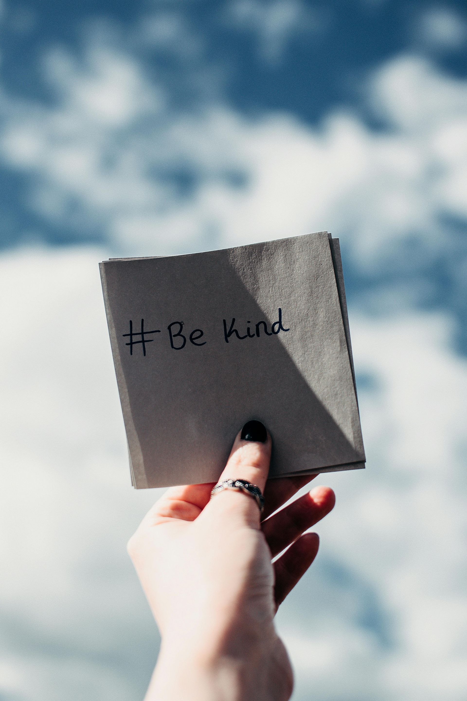 A person is holding a piece of paper that says be kind