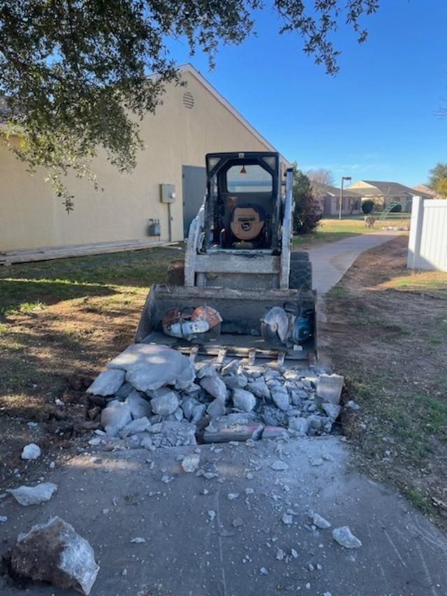 A bulldozer is working on a sidewalk in front of a house