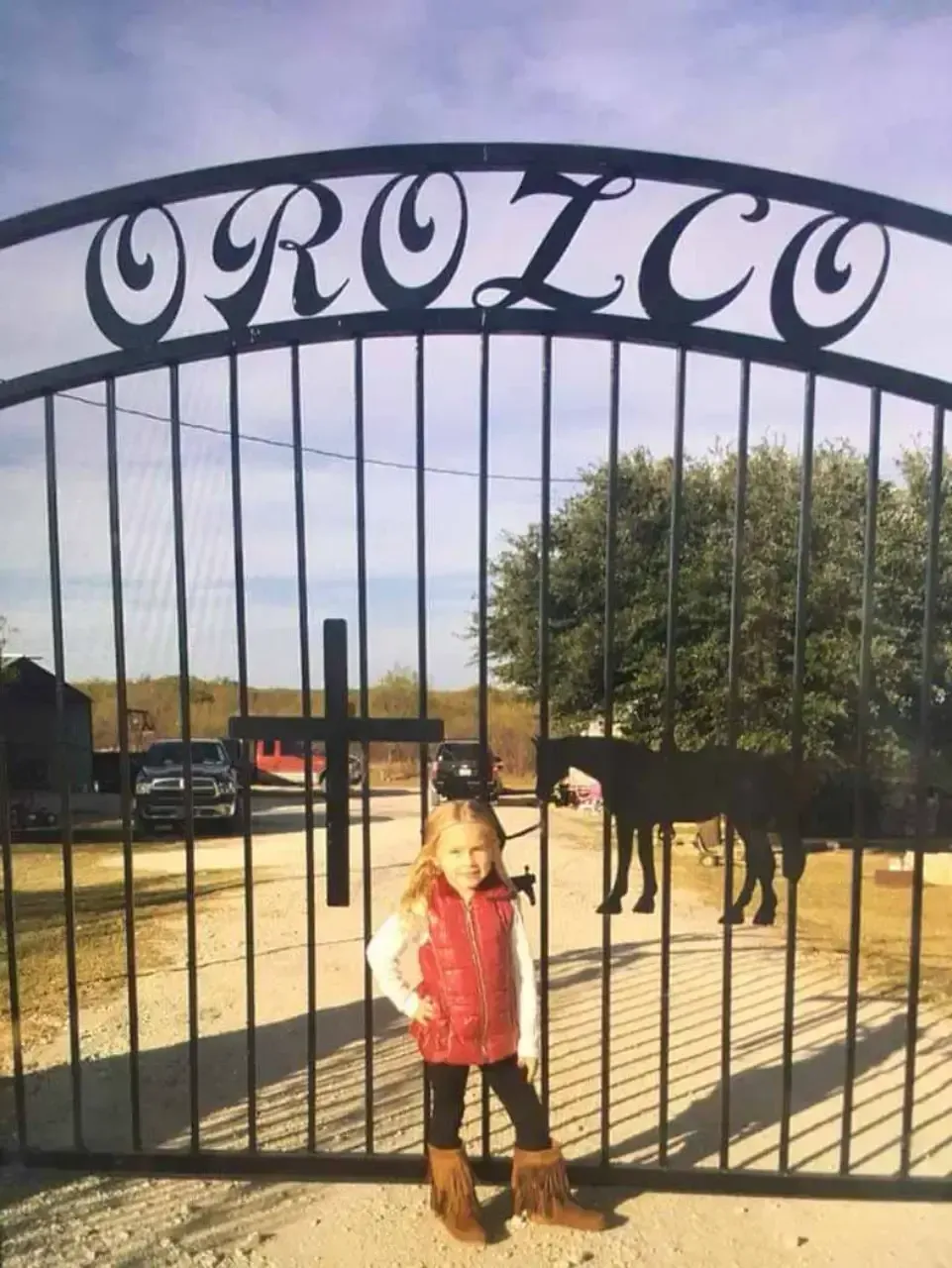 A little girl stands in front of a gate that says orozco