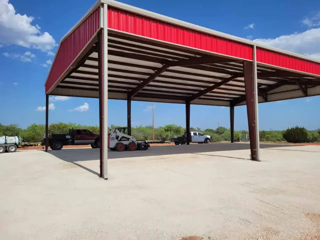 A bobcat is parked under a red roof in a parking lot.