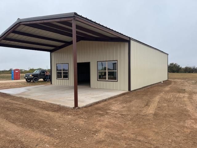 A car is parked under a canopy in front of a metal building.