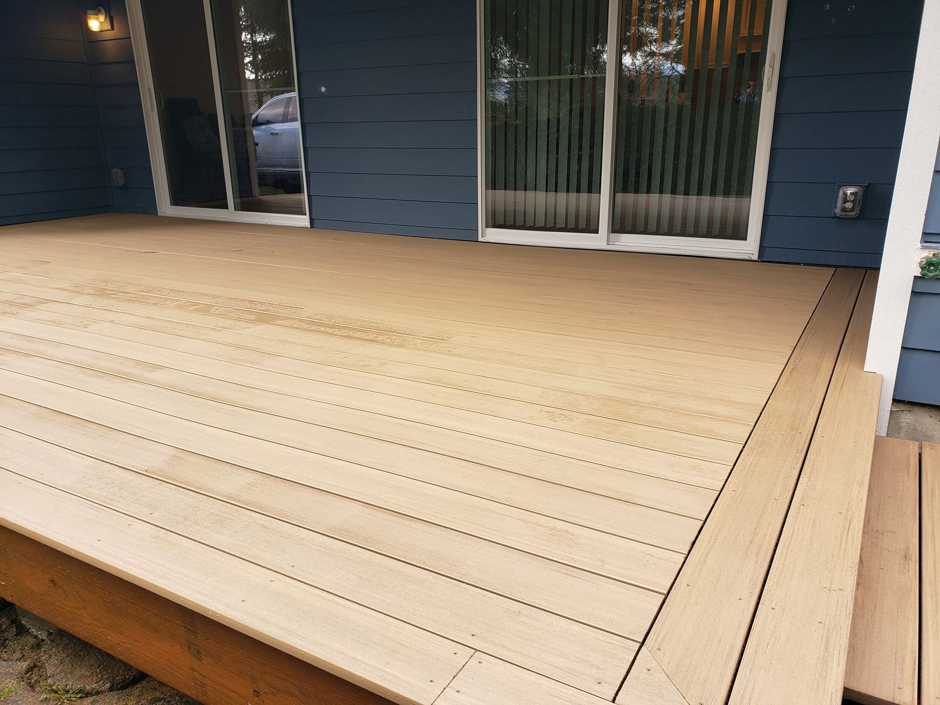 A wooden deck in front of a blue house with sliding glass doors.