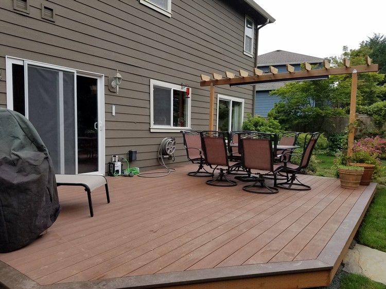 A deck with a table and chairs on it in front of a house.