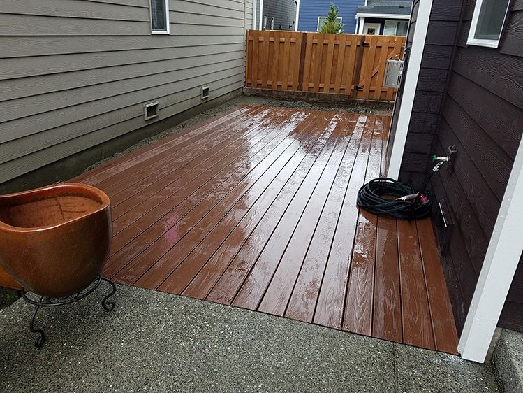 A wooden deck with a potted plant and a hose on it next to a house.