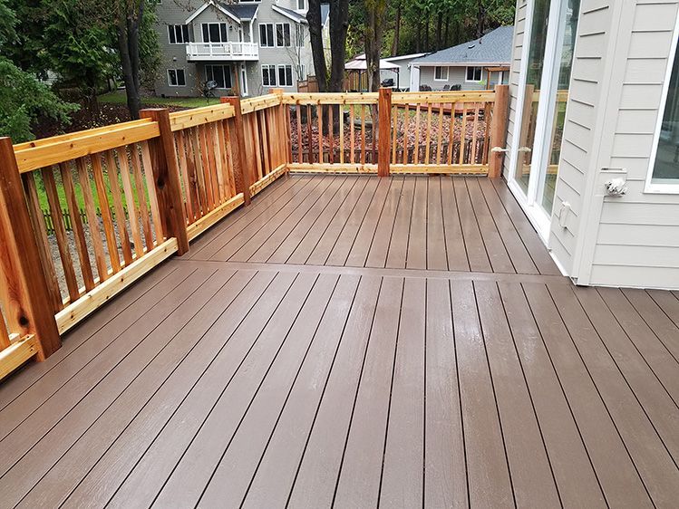 A large wooden deck with a wooden railing and a house in the background.