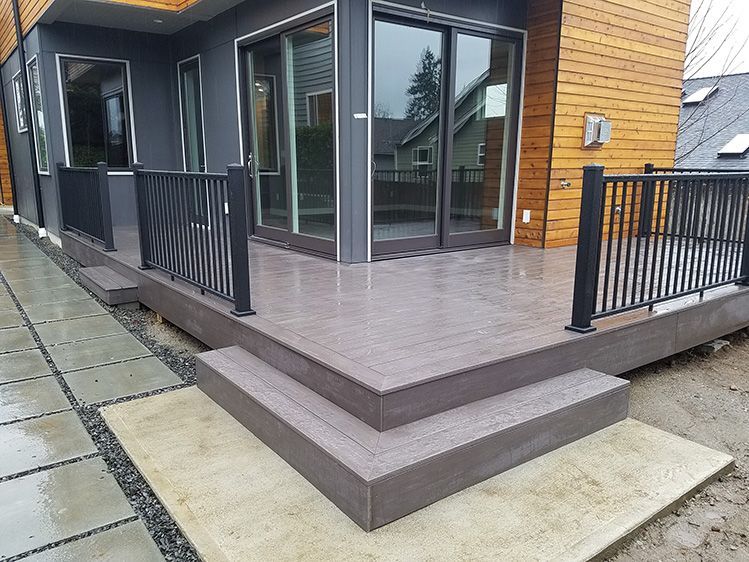 A deck with stairs and a railing in front of a house.