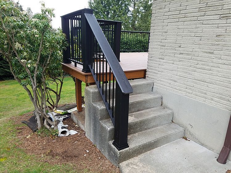 A deck with stairs leading up to it and a black railing.