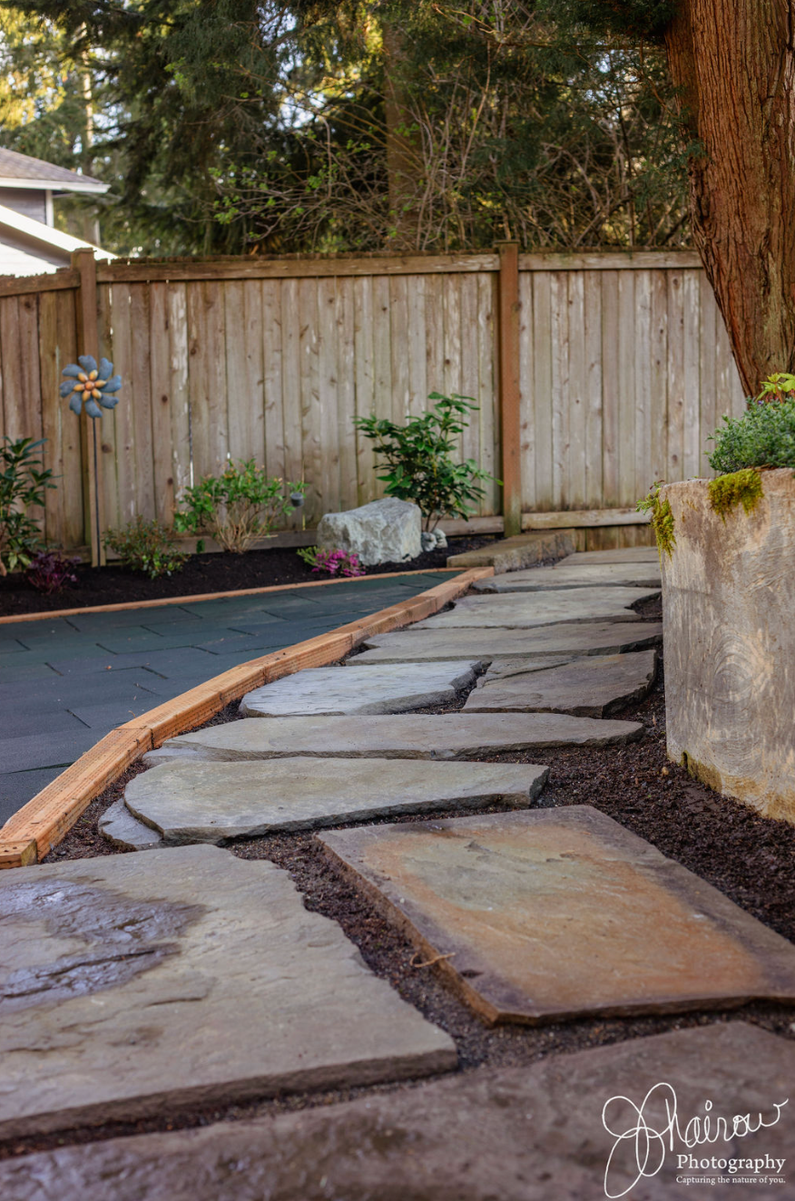 A stone walkway leading to a wooden fence in a backyard.