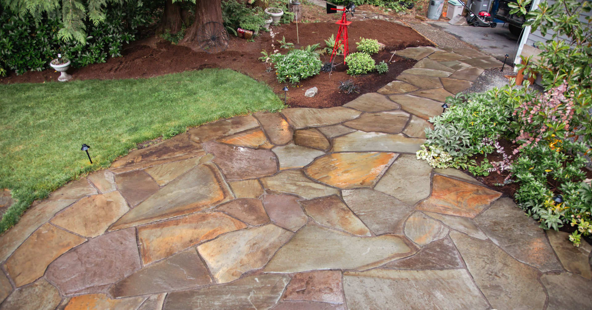 A stone walkway in a garden with a car parked in the background.