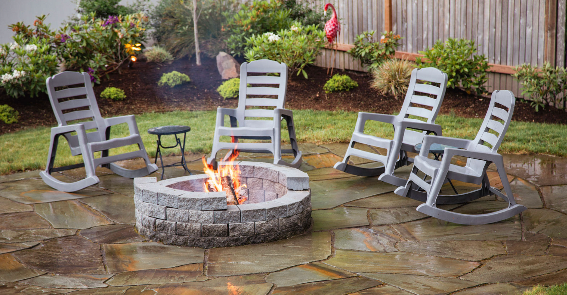 A fire pit with rocking chairs around it in a backyard.