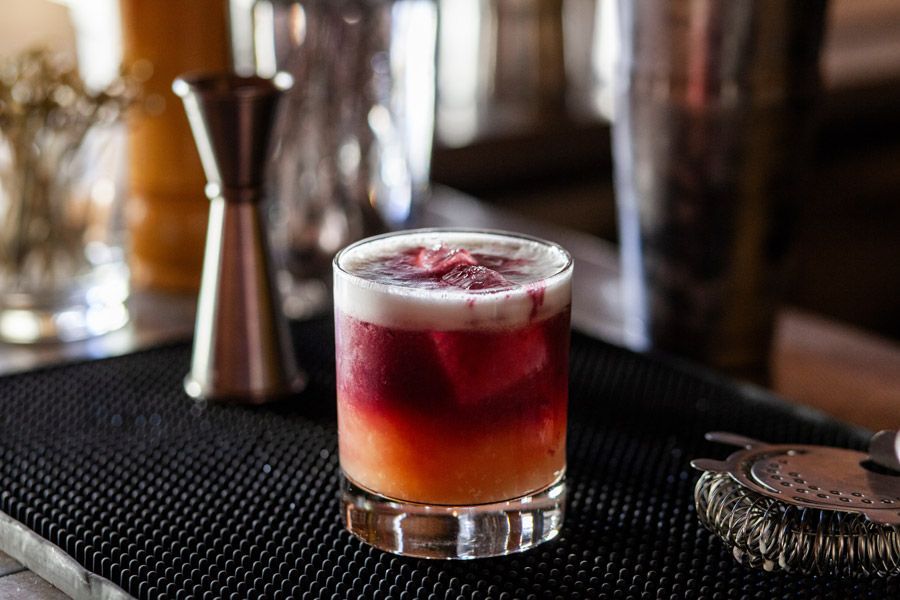 Cocktail in a glass, with layers of color and foamy top, on a bar setting with other bar tools.