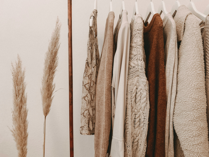 A light-filled room with clothes rack, stool, mirror, dried palm leaves, and a cabinet.