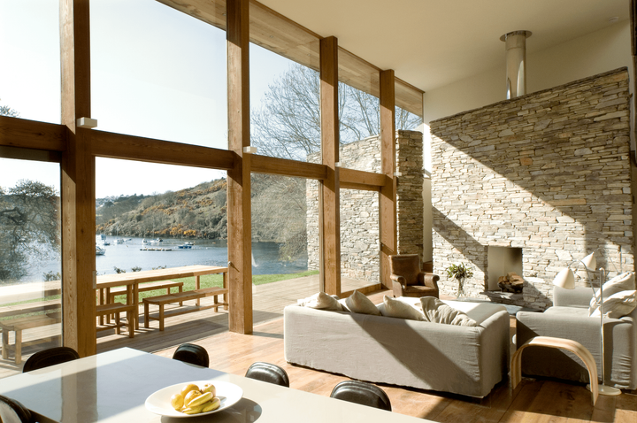Living room with large windows overlooking a lake, stone fireplace, and light-colored furniture.