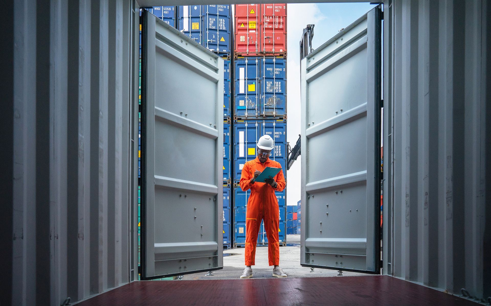 A man is standing in front of a stack of shipping containers.