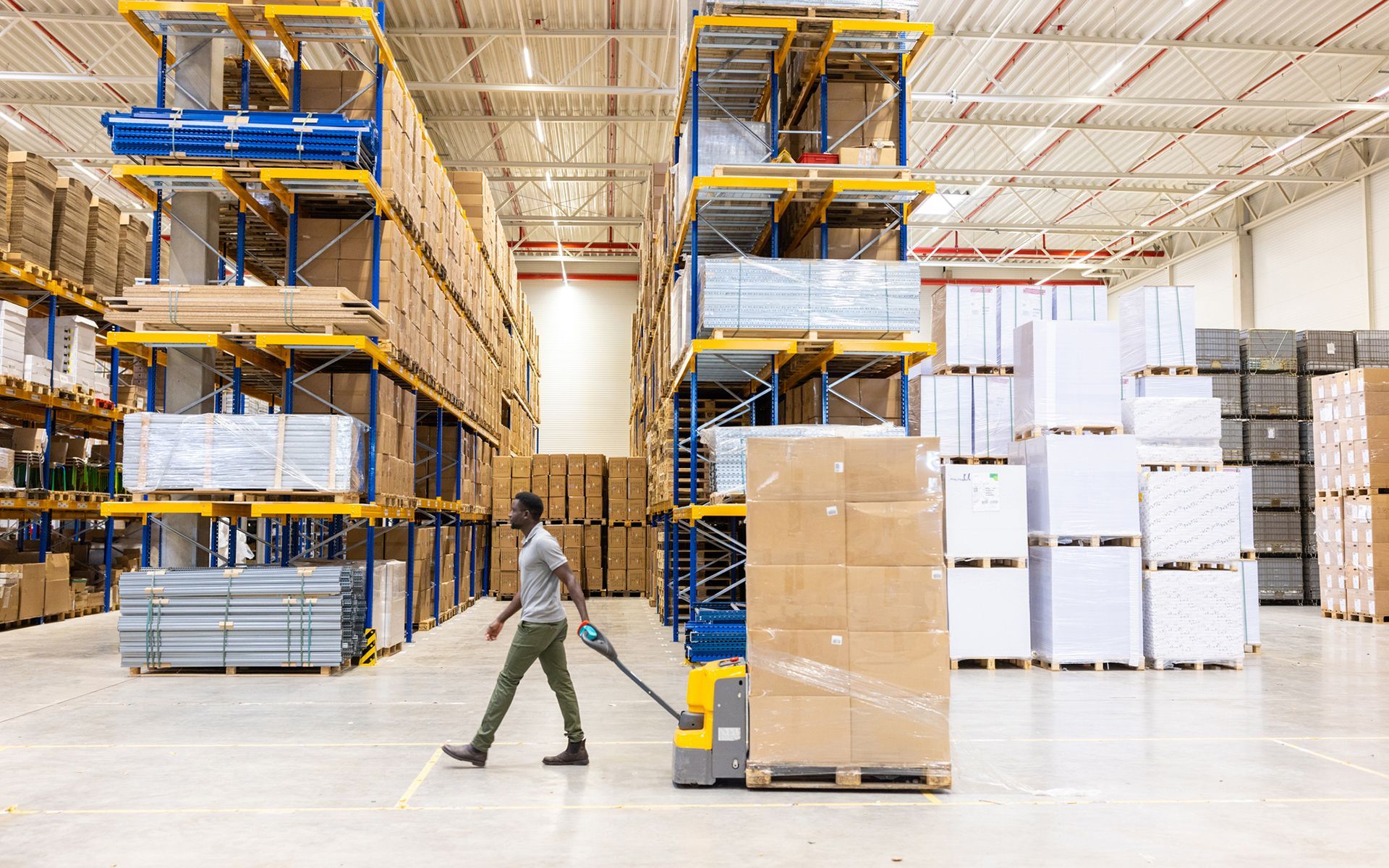 A man is pushing a pallet in a large warehouse.