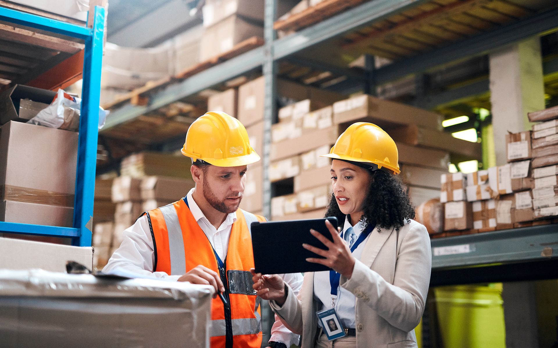 A man and a woman are looking at a tablet in a warehouse.