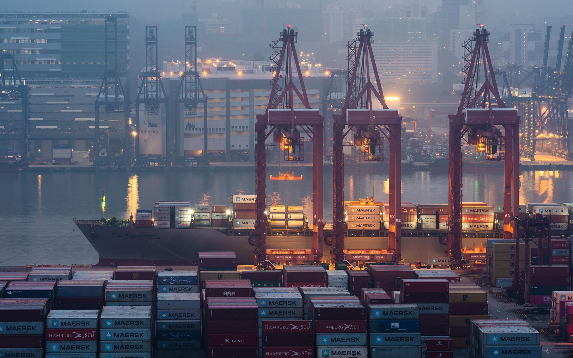 A large container ship is docked in a harbor at night.