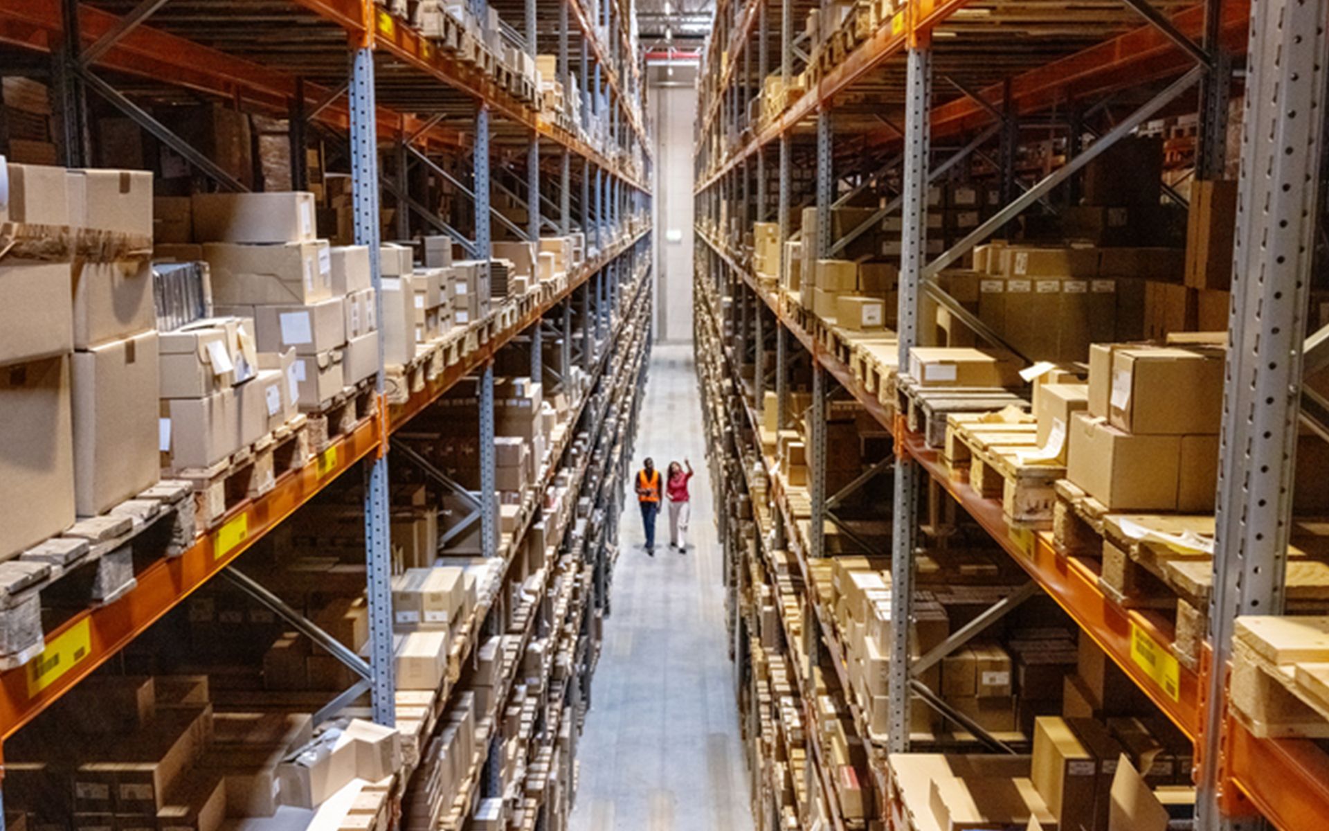 Two people are walking through a warehouse filled with lots of boxes.