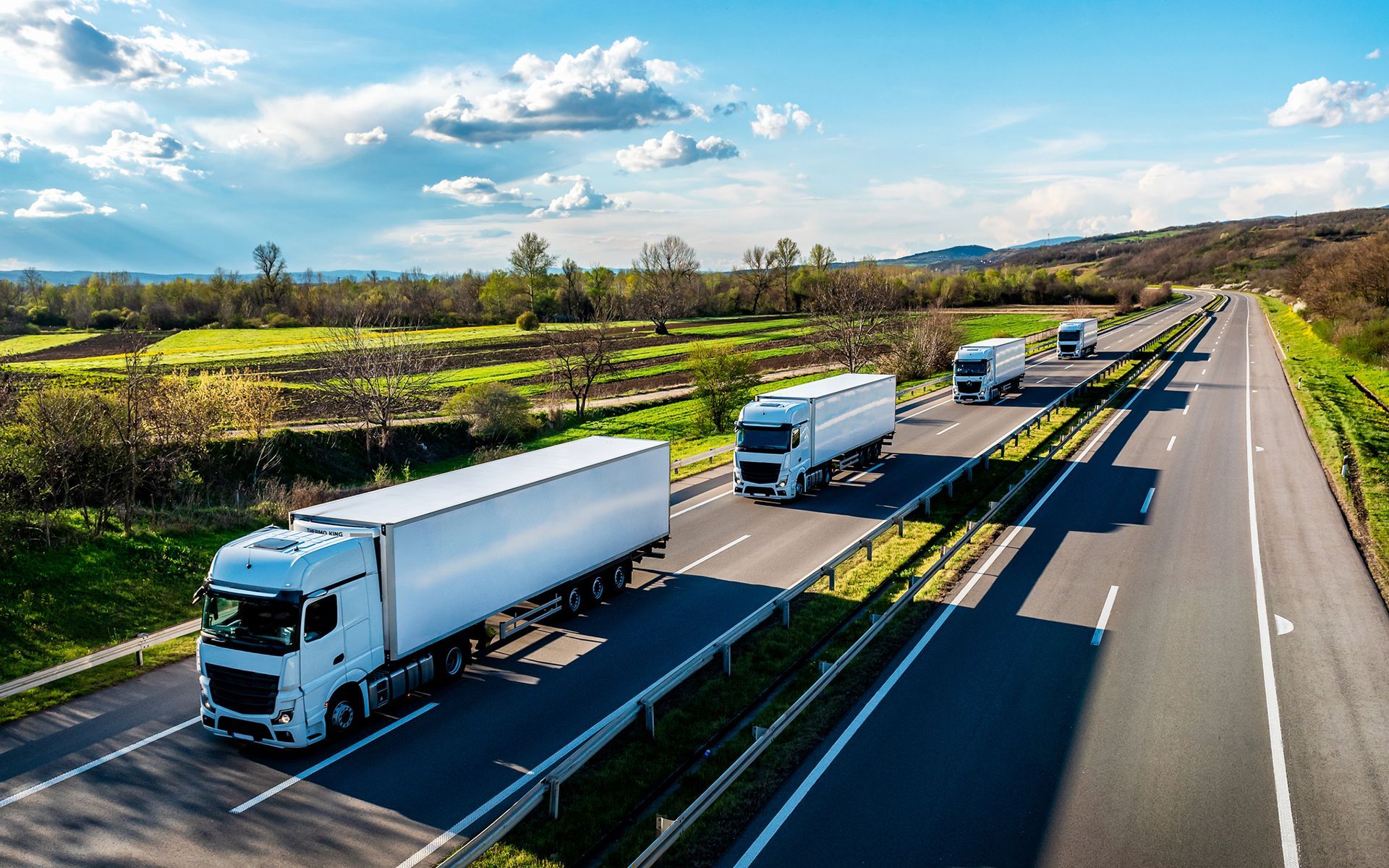 A row of white trucks are driving down a highway.