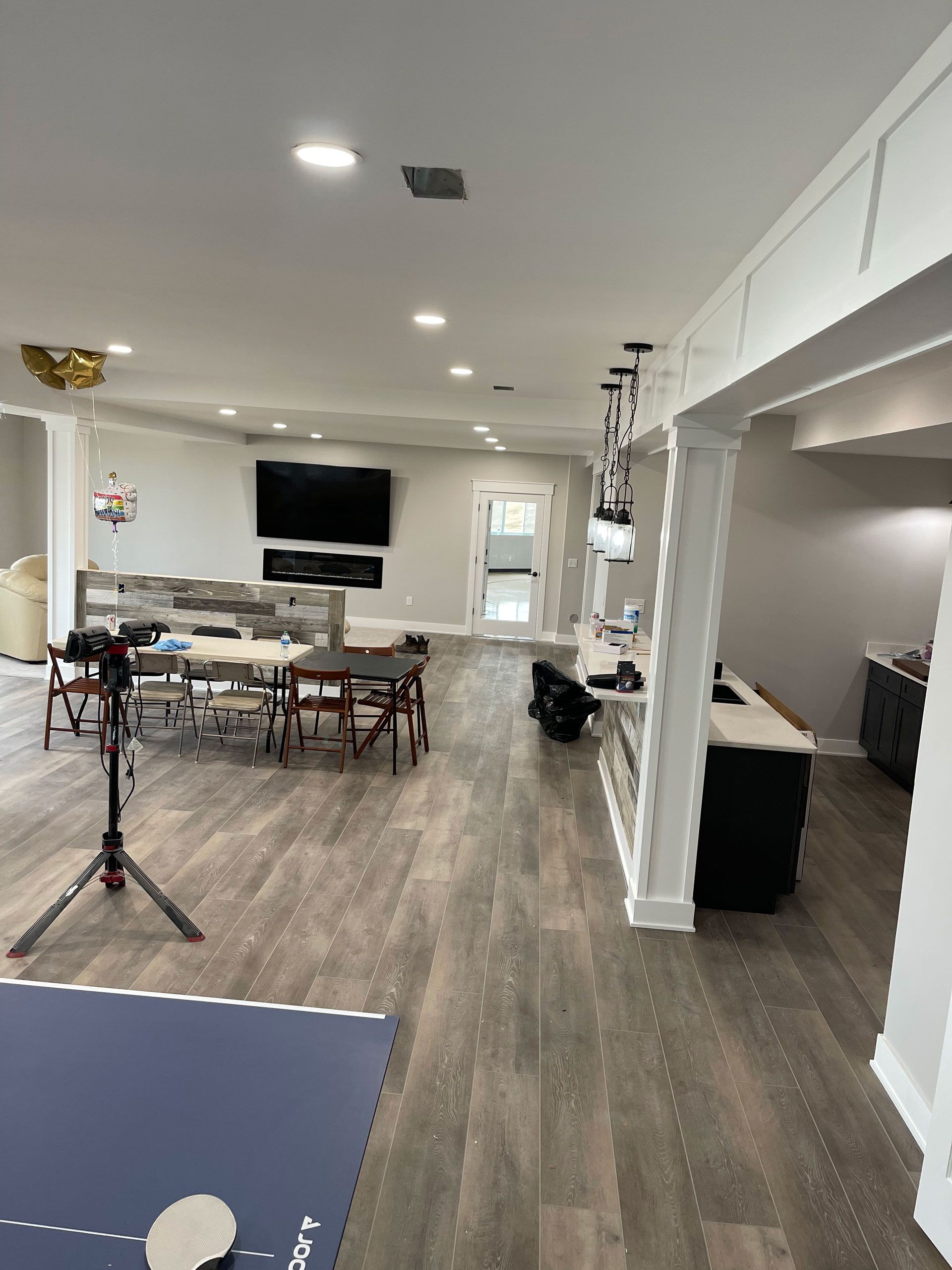A modern, open-concept living space with wood-look flooring, a dining area, a television, and a kitchen island.