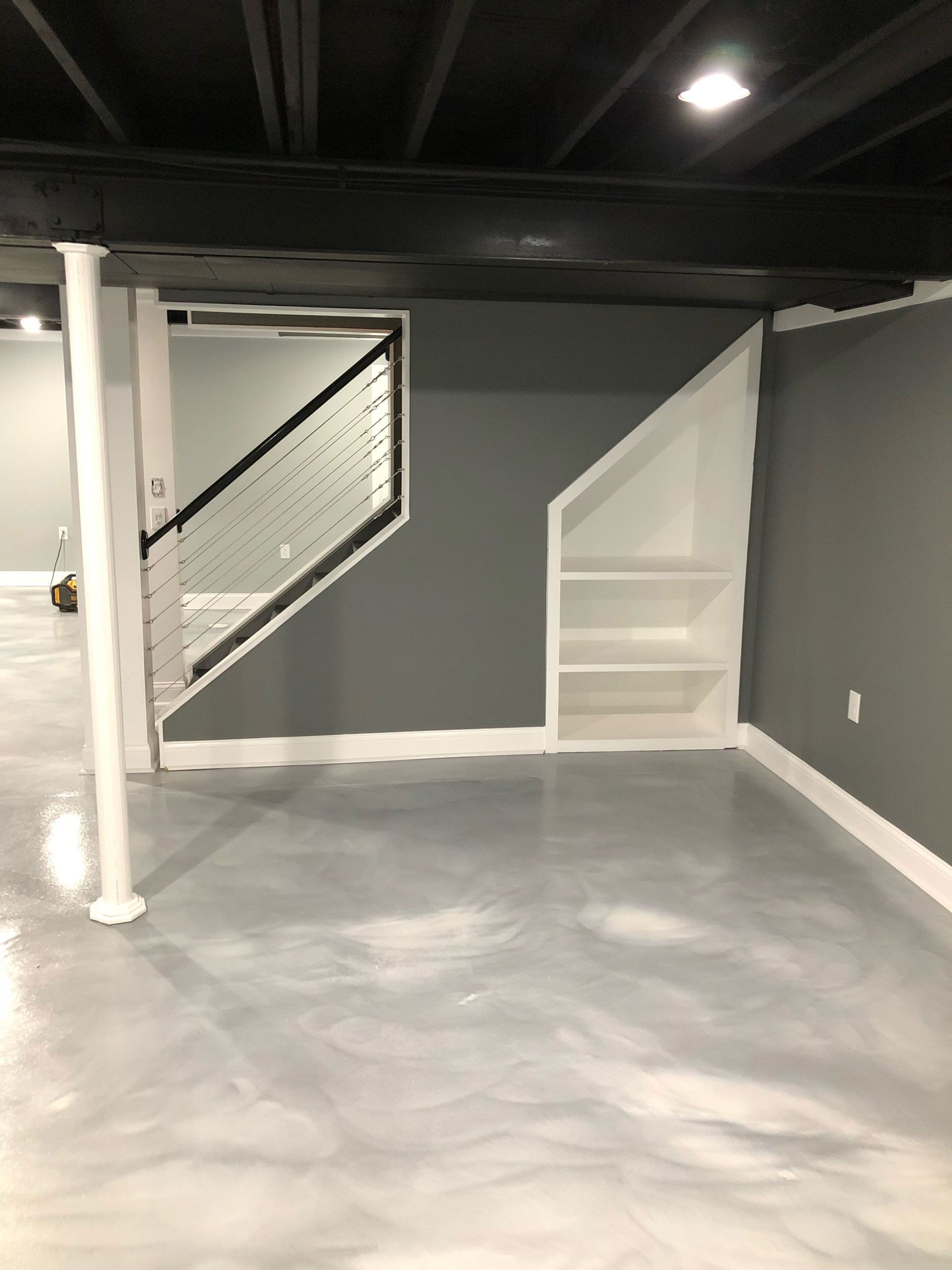A finished basement featuring dark gray walls, a glossy light gray floor, a built-in white bookshelf, and metal railing.