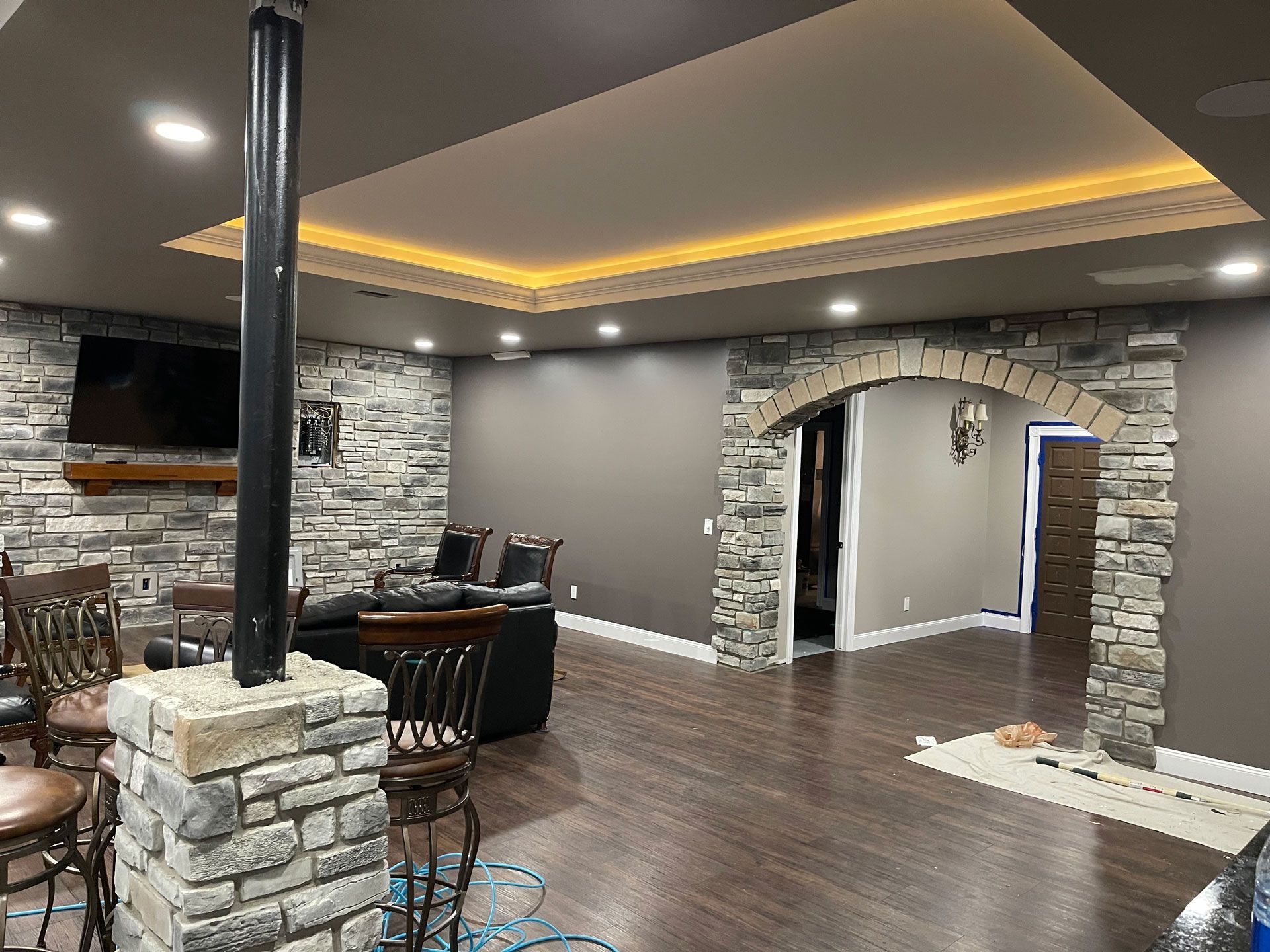 A basement featuring a stone column, a stone arched doorway, dark flooring, and a recessed ceiling with ambient lighting.