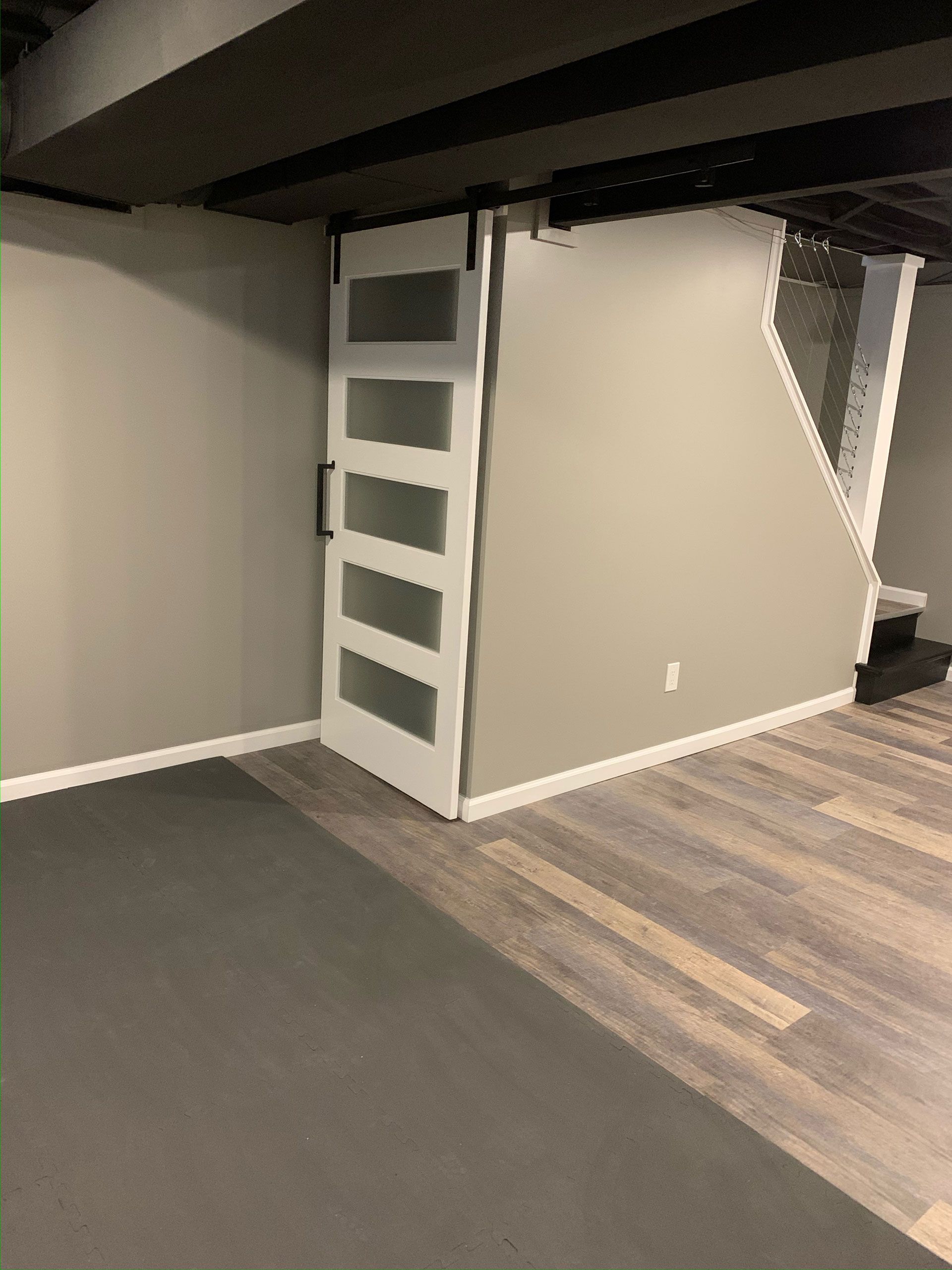 A white sliding barn door with five frosted glass panels installed on a grey wall next to a staircase in a basement.