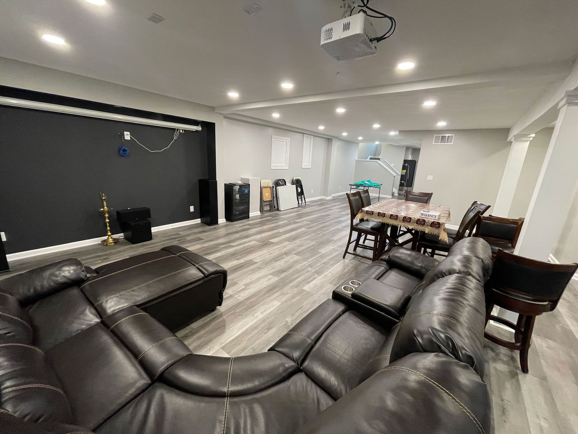 A spacious finished basement with a dark accent wall, a large brown sectional sofa, and a dining table with chairs.
