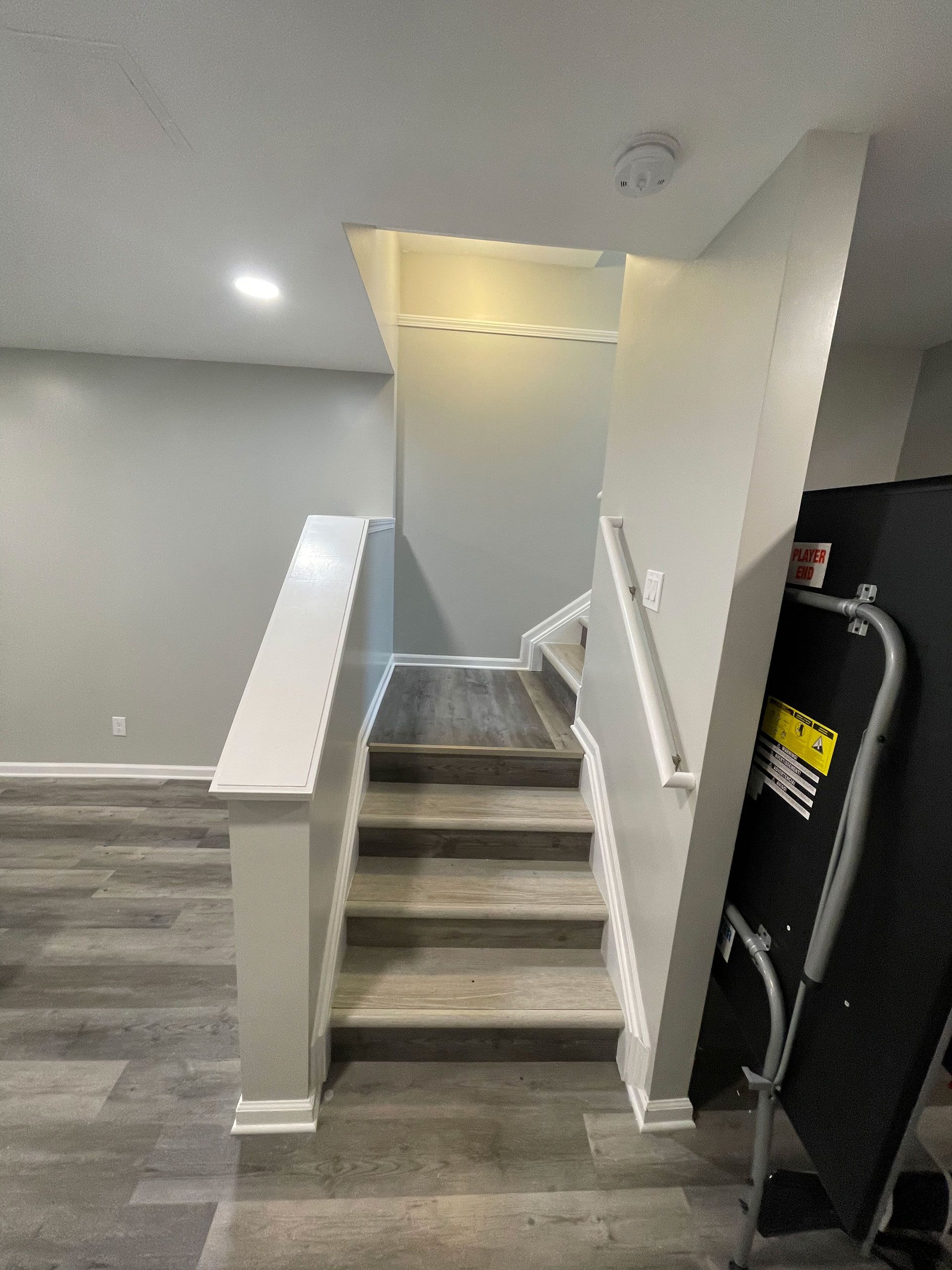 A set of interior wooden stairs with white railings leading upward in a room with light grey walls and grey wood flooring.