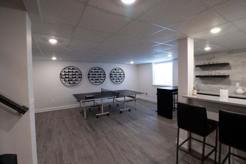 A finished basement with gray wood flooring, a ping-pong table, three circular wall shelves, and a small wet bar area.