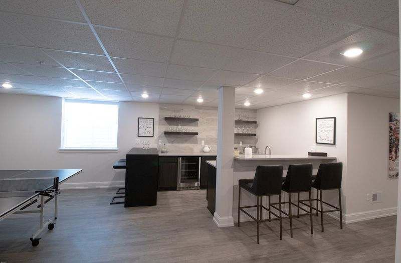 A finished basement with a kitchenette, bar seating, wood-look flooring, and a ping pong table under recessed lighting.