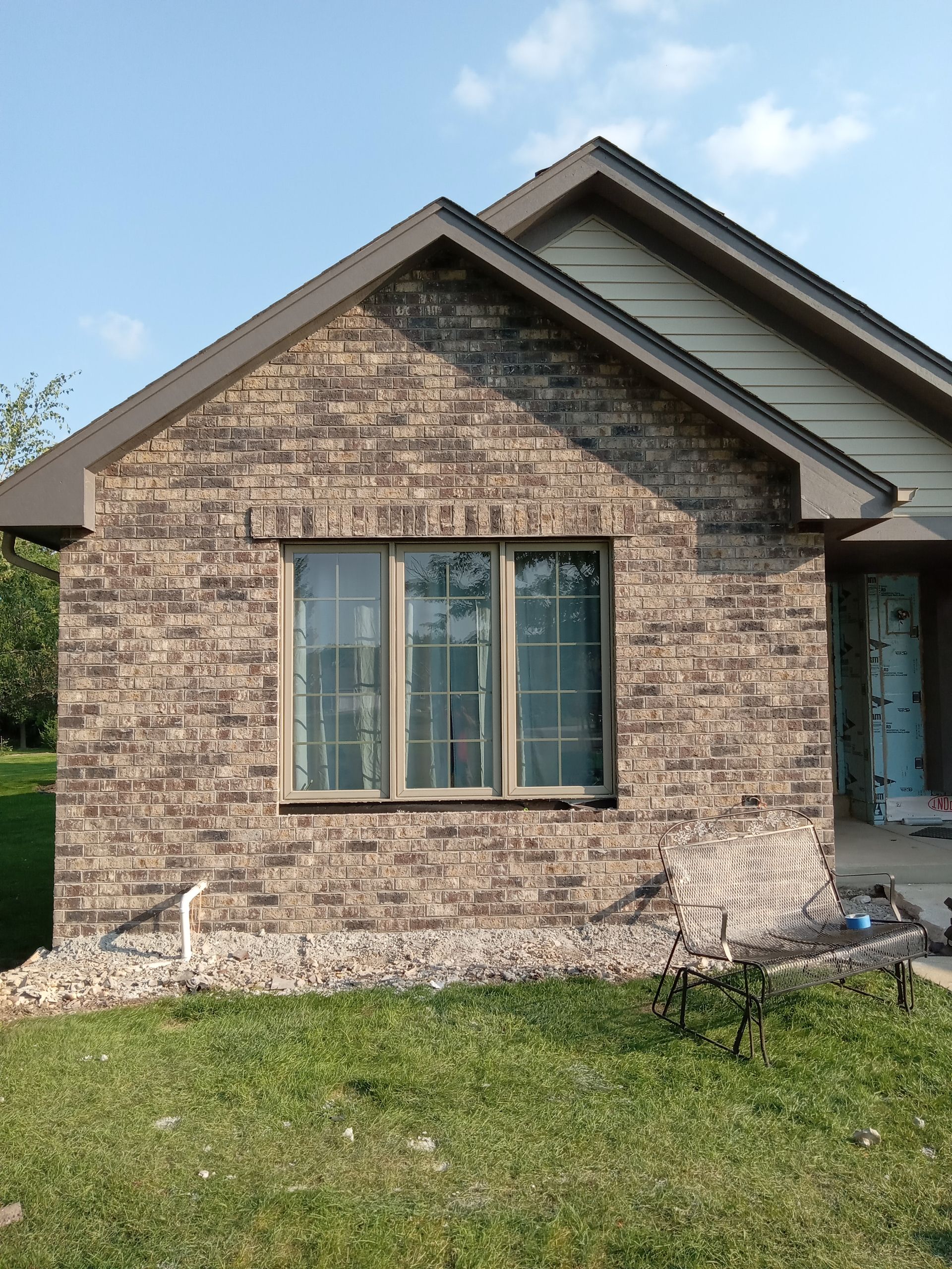 Brick house facade with a window, brown roofing, and a bench on the lawn.