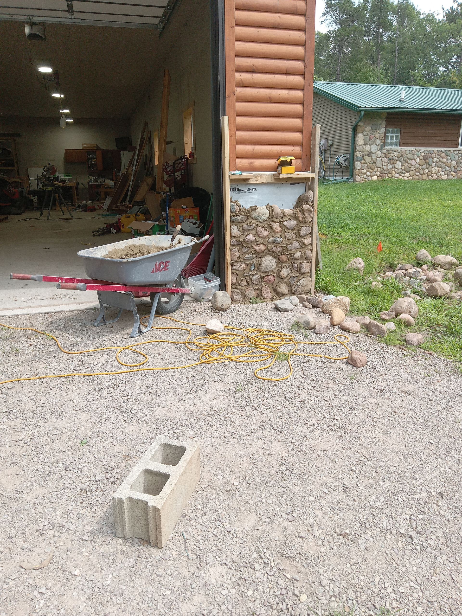 Construction site with a partially built stone wall next to a garage, materials and tools present.