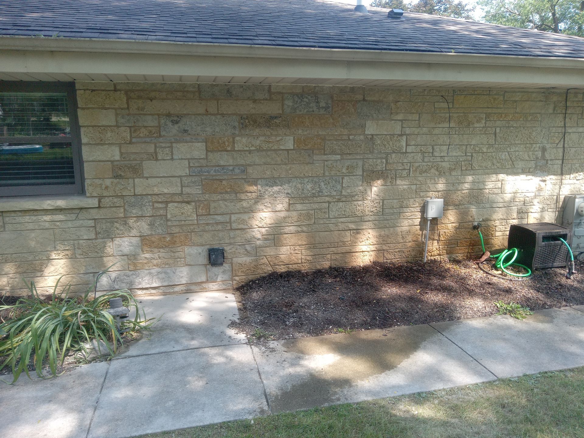 Stone brick house exterior with a window, electrical outlet, and garden hose.