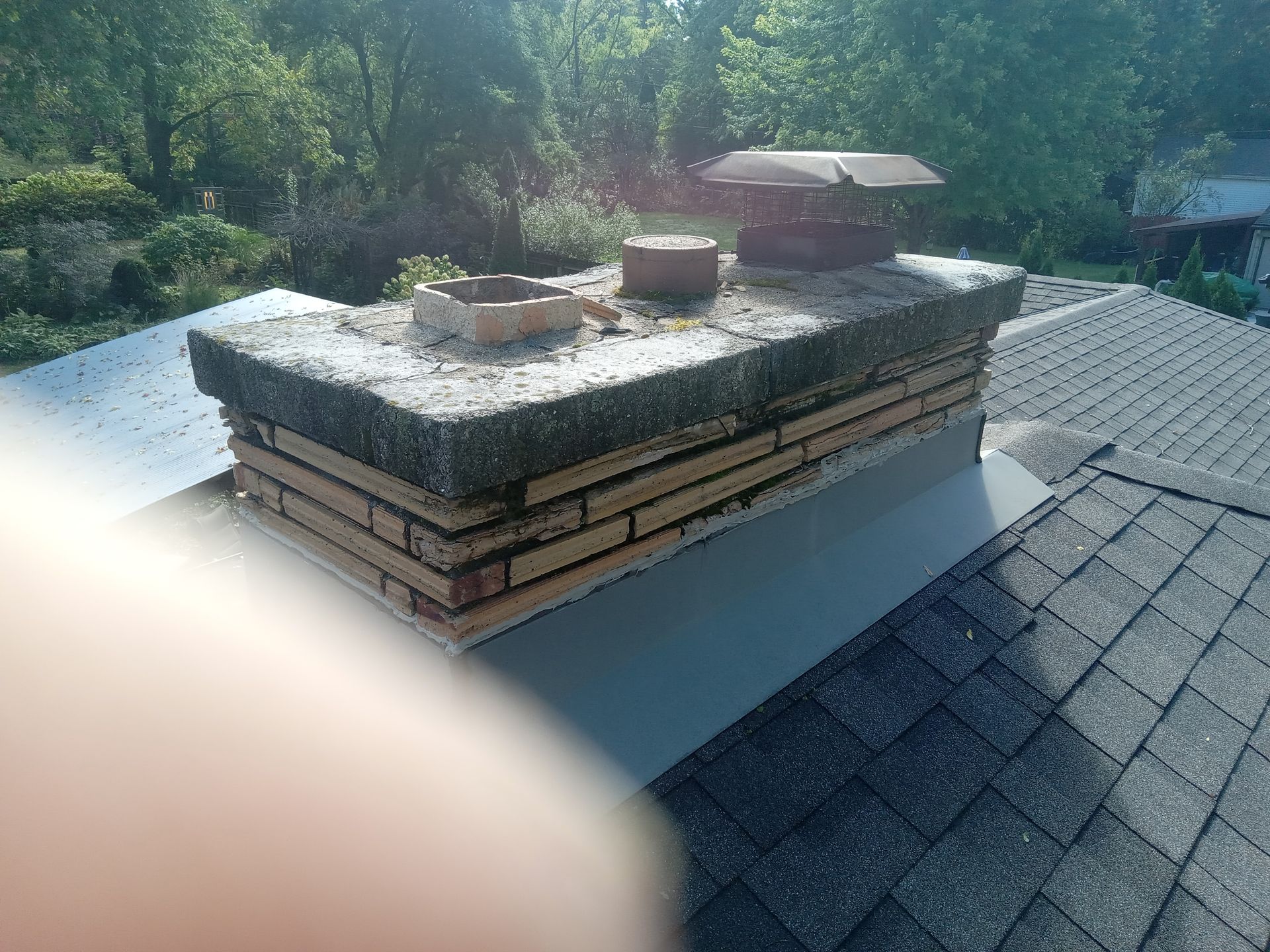 Chimney on a shingled roof with brickwork, concrete cap, and metal flashing.