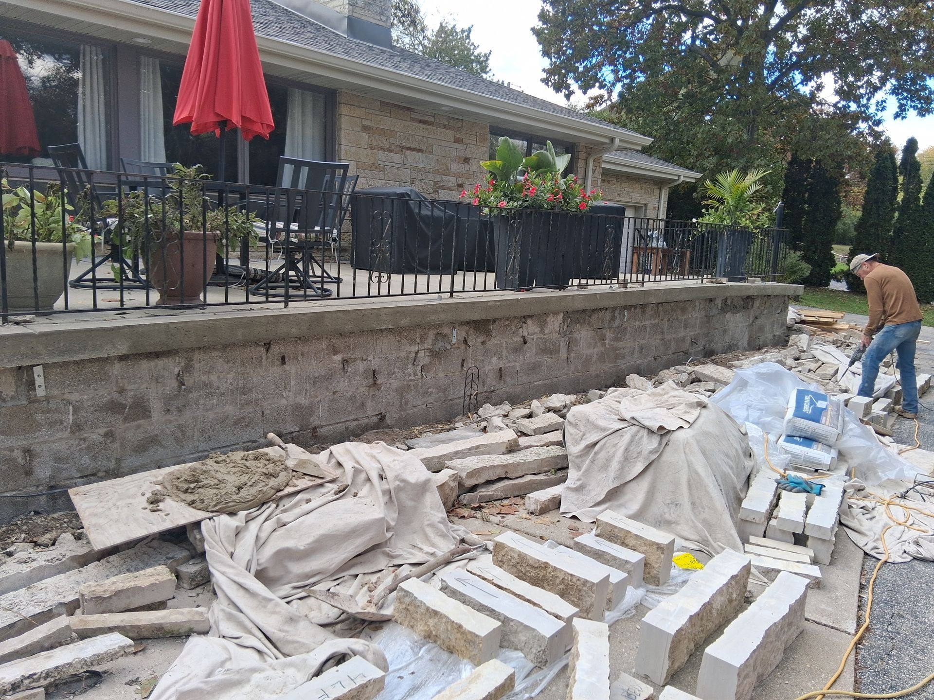 Man working on stone wall construction beside a house with a red umbrella.
