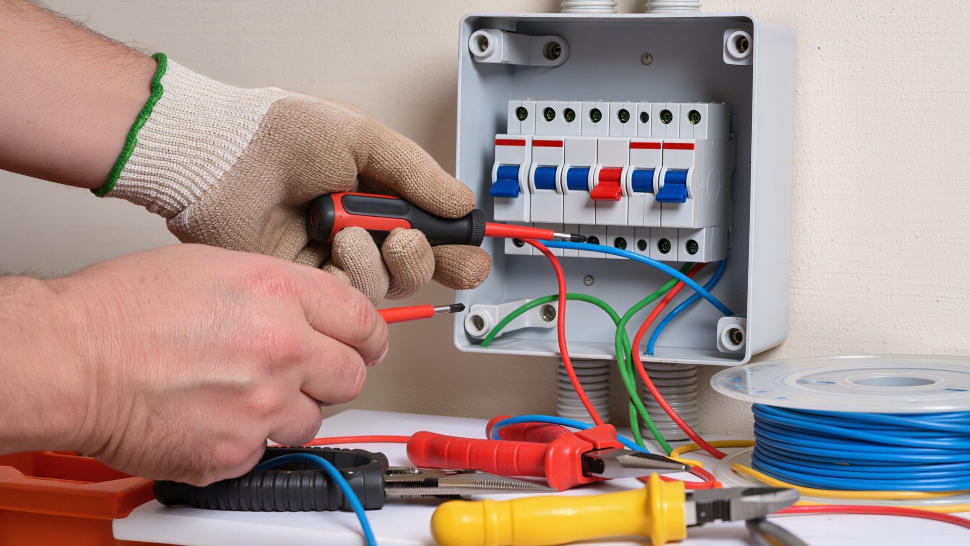 An electrician fixing an electrical grid. The open box is on the wall.